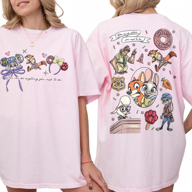 Puede incluir: Camiseta rosa claro con personajes de dibujos animados y la frase "You can be anything you wish to be". La parte trasera de la camiseta tiene gr&aacute;ficos de dibujos animados adicionales y las palabras "The Big Donut."