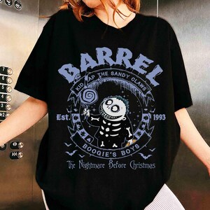 Op de afbeelding: Een zwart t-shirt met korte mouwen en een grafische print van het personage Barrel uit The Nightmare Before Christmas. Het ontwerp bevat de tekst BARREL, KIDNAP THE SANDY CLAWS, Est. 1993, BOOGIE'S BOYS en The Nightmare Before Christmas.