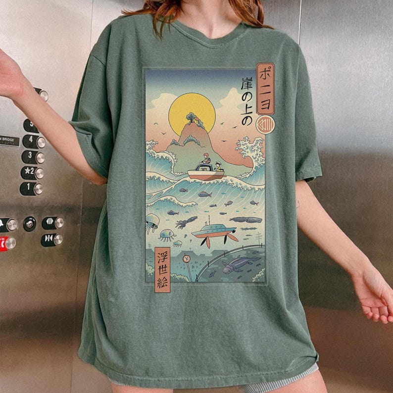 May include: Sage green t-shirt featuring a Japanese-inspired graphic. The design depicts a boat on a wave, a rising sun, and Japanese text. The shirt has short sleeves and a relaxed fit.
