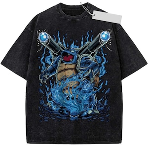 May include: A black acid-wash t-shirt featuring a graphic illustration of a blue turtle-like creature with two large cannons on its back, surrounded by blue flames and water effects, with a blank white rectangular price tag attached to the collar.