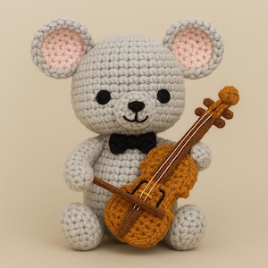 Peut inclure: Une souris grise au crochet avec des oreilles intérieures roses et un nœud papillon noir, tenant un petit violon au crochet marron et orange. Le jouet est fait à la main et a des yeux noirs en forme de bouton.