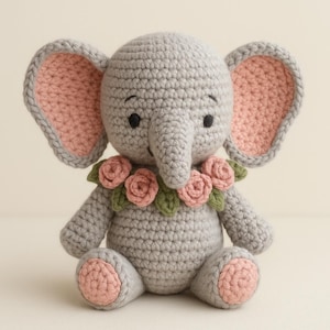 May include: A crocheted grey elephant toy with pink accents on the ears and feet. The elephant has a floral collar of pink roses and green leaves. The toy is sitting upright with its trunk extended.