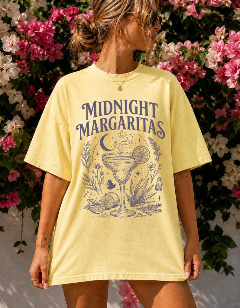 K&ouml;nnte beinhalten: Ein hellgelbes Kurzarm-T-Shirt mit einem dunkelblauen Grafikdruck. Das Design zeigt den Schriftzug "MIDNIGHT MARGARITAS" &uuml;ber einer Illustration eines Margaritaglases, einer Mondsichel, Sternen, Limettenscheiben und botanischen Elementen.