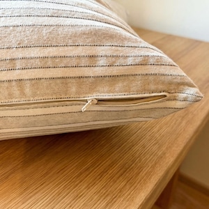 Nahaufnahme des verdeckten, farblich passenden Reißverschlusses an der beige-grau gestreiften Kissenhülle; Gewebe, Naht und Verarbeitung sind sichtbar.