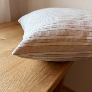 Seitliche Nahaufnahme der gefüllten Kissenhülle auf einem Holztisch; Kante, Volumen und gestreifte Webstruktur sind sichtbar.