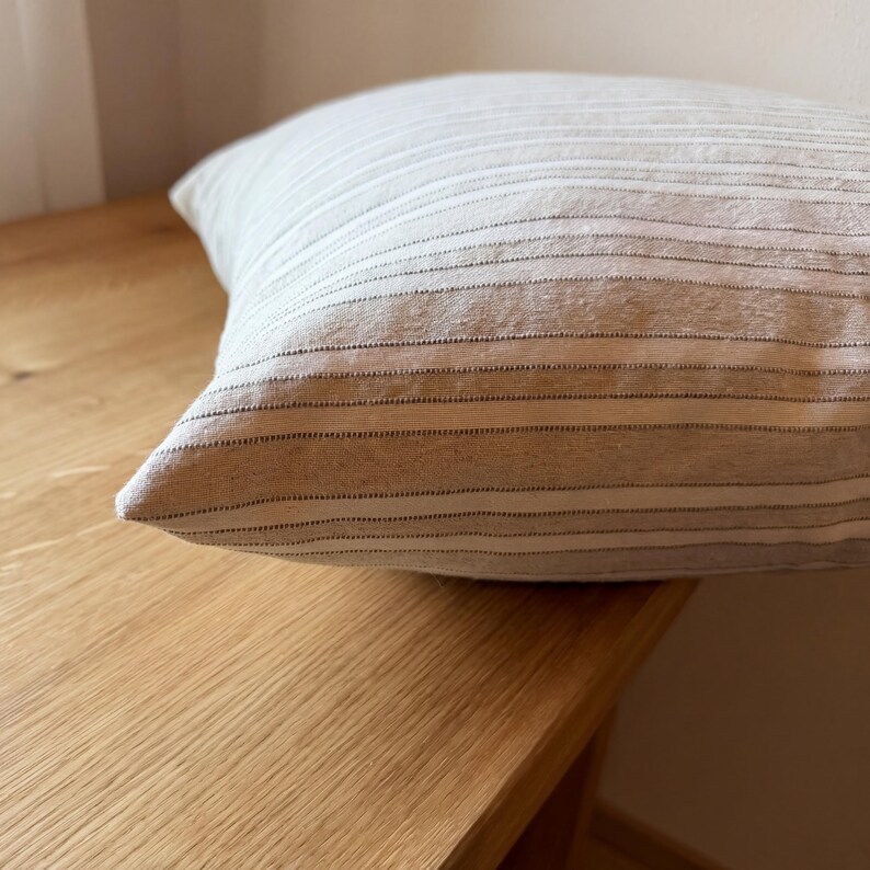 Seitliche Nahaufnahme der gefüllten Kissenhülle auf einem Holztisch; Kante, Volumen und gestreifte Webstruktur sind sichtbar.