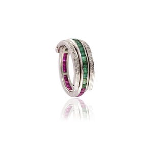 May include: A silver ring with three bands. The top band is encrusted with small diamonds, the middle band with green emeralds, and the bottom band with red rubies. The ring is set against a white background.