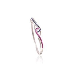 May include: A silver bracelet with a curved design. The bracelet features a series of small, square-cut gemstones in blue, pink, and clear colors. The gemstones are set in a wave-like pattern, creating a visually appealing and elegant piece of jewelry.