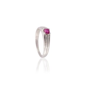 Puede incluir: Un anillo de plata con una gema rosa brillante de forma cuadrada. El anillo tiene una banda sencilla que se ensancha ligeramente hacia la parte superior, con ranuras verticales a cada lado del engaste de la gema. La gema es el punto focal del anillo.