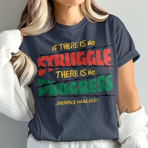 Könnte beinhalten: Marineblaues T-Shirt mit dem Zitat "Wenn es keinen Kampf gibt, gibt es keinen Fortschritt" in Rot, Gelb und Grün, mit Stacheldraht-Akzenten. Das Zitat stammt von Frederick Douglass.