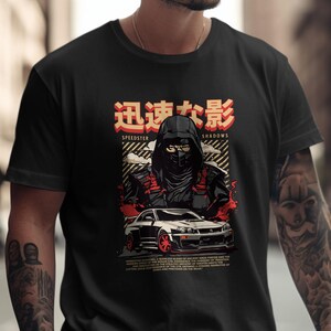 Könnte beinhalten: Schwarzes T-Shirt mit einer Grafik einer Kapuzenfigur, eines Sportwagens und japanischem Text. Das Design enthält rote und weiße Akzente. Das Thema des T-Shirts ist Geschwindigkeit und Schatten.