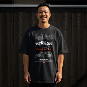 May include: Black t-shirt featuring a Bugatti Veyron design. The graphic includes blueprints and an image of the car in black and orange. The text "BUGATTI VEYRON" is prominently displayed. The shirt is worn by a person.