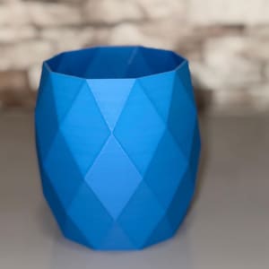Könnte beinhalten: Ein blauer geometrischer Pflanzentopf mit facettiertem Design. Der Pflanzentopf hat einen lebendigen Blauton und eine zylindrische Form mit einer breiten Öffnung. Die Oberfläche besteht aus rautenförmigen Facetten.