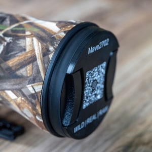 Könnte beinhalten: Ein Objektiv mit Tarnmuster und schwarzem Endkappe. Auf der Endkappe steht "Mave2702" und ein QR-Code. Das Objektiv ist für den Außeneinsatz konzipiert und hat ein robustes Aussehen.