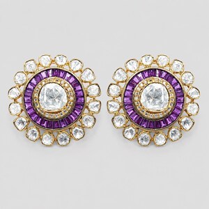 May include: A pair of circular gold earrings featuring a central rose-cut white stone surrounded by a ring of baguette-cut purple stones, an inner border of small white stones, and an outer halo of larger rose-cut white stones in gold settings.
