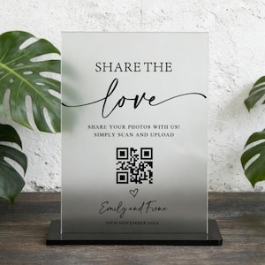 May include: A rectangular frosted acrylic sign with black text and a QR code. The sign reads SHARE THE LOVE, SHARE YOUR PHOTOS WITH US! SIMPLY SCAN AND UPLOAD, followed by a heart icon, the names Emily and Fiona, and the date 18TH NOVEMBER 2024.