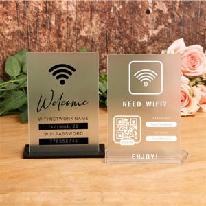 Könnte beinhalten: Zwei rechteckige Schilder aus mattiertem Acryl mit schwarz-weißem Aufdruck. Das linke Schild zeigt ein WLAN-Symbol, das Wort Welcome und Netzwerkdaten. Das rechte Schild enthält ein WLAN-Symbol, einen QR-Code sowie Felder für Netzwerkdaten.