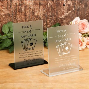 Op de afbeelding: Twee heldere acryl borden met de tekst "PICK A card ANY CARD" en een speelkaarten ontwerp. De borden bevatten ook de tekst "PLEASE WRITE A MESSAGE AND SIGN YOUR NAME, SO WE CAN REMEMBER THIS SPECIAL DAY ANY TIME WE PLAY!" en een datum.
