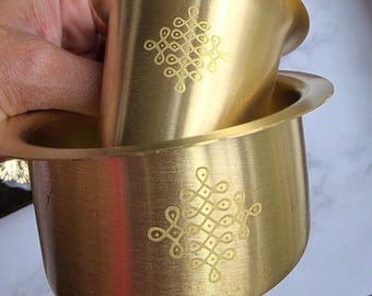 May include: A set of two brass coffee filters. The filters are gold-colored and feature an etched design. The top filter is nested inside the bottom filter. The filters are designed for brewing coffee.