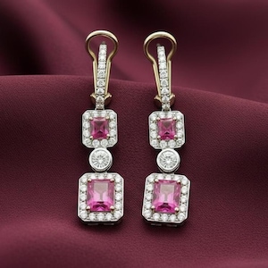 May include: A pair of elegant drop earrings featuring square pink gemstones surrounded by a halo of smaller white stones. The earrings have a gold-colored top and are set against a deep red background.
