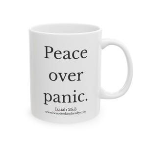 May include: White ceramic mug with the words "Peace over panic" in black, along with the Bible verse Isaiah 26:3 and the website www.berootedandready.com. The mug has a curved handle.
