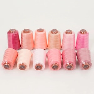 May include: Ten spools of thread in a range of pink and peach hues. The spools are arranged in two rows, with the top row standing upright and the bottom row lying horizontally. Each spool is wrapped in clear plastic, ready for use.