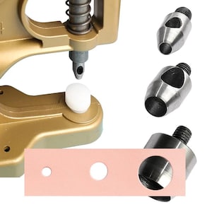 May include: A gold-colored press with a spring and a white plastic base. Three silver metal hole punch attachments are shown, along with a pink leather strip with three different sized holes punched into it. The tools are for leathercraft.