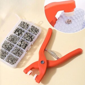 May include: An orange snap fastener tool with a spring and a clear plastic container filled with silver snaps. A close-up shows the tool in use, attaching a snap to fabric. The tool is approximately 8 inches long.