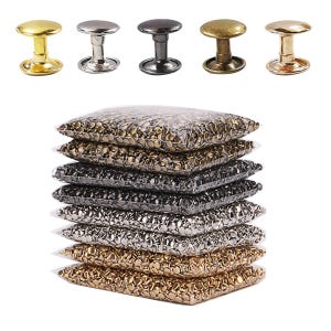 Op de afbeelding: Een assortiment metalen klinknagels in diverse kleuren, waaronder goud, zilver en gunmetal, weergegeven boven verschillende transparante plastic zakken gevuld met klinknagels. Voor leerbewerking, kleding en doe-het-zelf projecten.