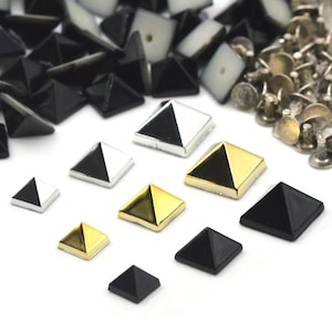 May include: A collection of pyramid-shaped studs in various colors, including black, silver, and gold. Some studs are two-toned, with a black and silver design. Also visible are silver-colored rivets, suitable for leathercraft or garment embellishment.