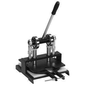 Puede incluir: Máquina manual para hacer botones en negro y plata. La máquina tiene un mango largo plateado con agarre negro, una base negra y un área de matriz circular. La máquina tiene varios componentes plateados y negros.