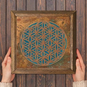 May include: Square framed artwork featuring a teal and gold geometric design. The artwork has a textured, aged appearance with a wooden frame. The central design is a detailed pattern of interlocking shapes.