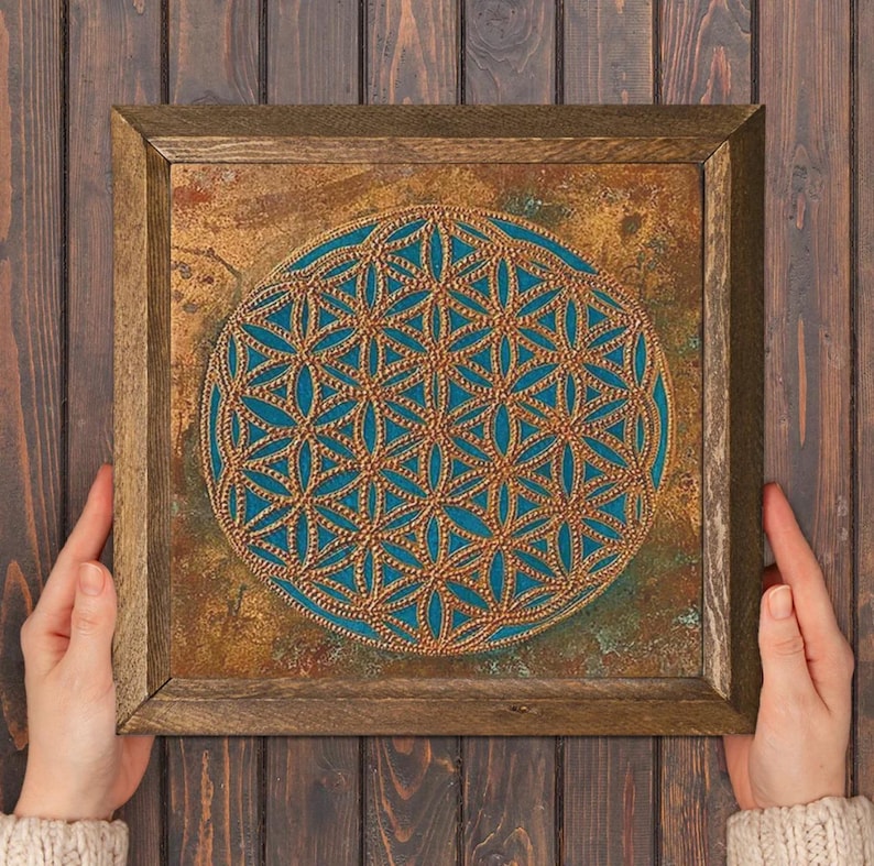 May include: Square framed artwork featuring a teal and gold geometric design. The artwork has a textured, aged appearance with a wooden frame. The central design is a detailed pattern of interlocking shapes.