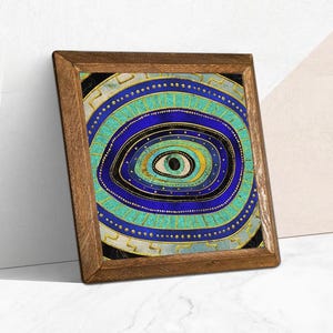 May include: A framed art print with an abstract eye design. The artwork uses concentric circles in blue, teal, and gold, with a black pupil. The wooden frame complements the vibrant colours of the artwork.