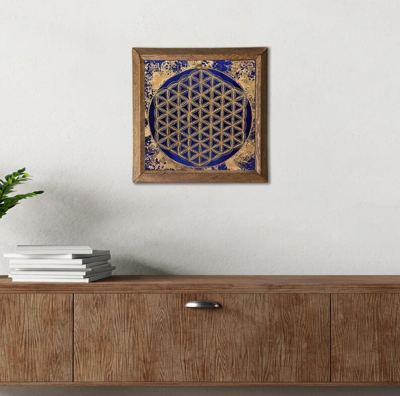 K&ouml;nnte beinhalten: Ein gerahmtes Kunstwerk mit einem goldenen geometrischen Muster, der Blume des Lebens, vor einem tiefblauen Hintergrund. Das Kunstwerk ist in einem Holzrahmen eingefasst und erzeugt einen auff&auml;lligen Kontrast.