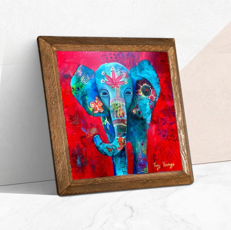 Puede incluir: Una impresi&oacute;n art&iacute;stica enmarcada que presenta un elefante vibrante y estilizado sobre un fondo rojo. El elefante est&aacute; pintado en tonos azules, adornado con patrones florales y de hojas. El marco de madera a&ntilde;ade un toque r&uacute;stico a la obra.