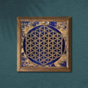 K&ouml;nnte beinhalten: Ein gerahmtes Kunstwerk mit einem goldenen und blauen geometrischen Design, der Blume des Lebens, auf einem strukturierten Hintergrund. Das Kunstwerk ist in einem Holzrahmen eingefasst und eignet sich f&uuml;r die Inneneinrichtung.