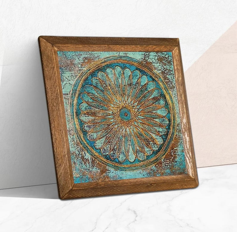 K&ouml;nnte beinhalten: Quadratische Holzrahmen-Kunst mit einem t&uuml;rkis-goldenen Blumendesign. Das Kunstwerk hat ein verwittertes, strukturiertes Aussehen. Der Rahmen besteht aus Naturholz. Das Kunstwerk lehnt an einer wei&szlig;en Wand.