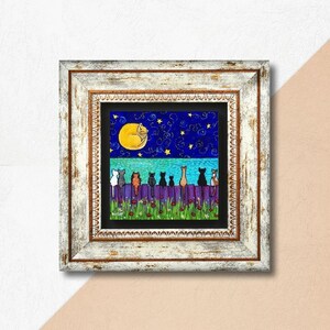 May include: A framed art print depicts a whimsical night scene. A yellow moon with a sleeping cat hangs in a starry blue sky above a purple fence. Several cats of various colors sit on the fence, with red flowers below.