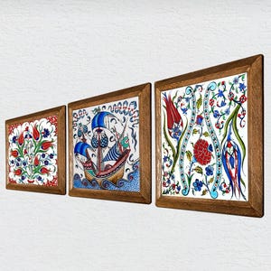 Puede incluir: Tres azulejos de cerámica enmarcados con intrincados diseños florales y de barcos. Los azulejos presentan colores vibrantes, incluyendo rojo, azul y verde, sobre un fondo blanco. Cada azulejo está encerrado en un marco de madera, creando un conjunto decorativo de arte mural.
