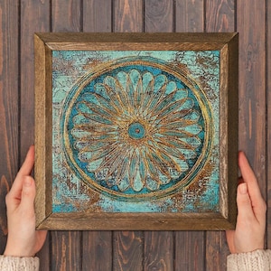 K&ouml;nnte beinhalten: Quadratische gerahmte Kunst mit einem t&uuml;rkis-goldenen Blumendesign. Das Kunstwerk zeigt ein zentrales bl&uuml;tenartiges Motiv mit komplizierten Details und einem strukturierten, verwitterten Hintergrund. Der Rahmen besteht aus Naturholz.