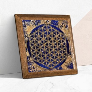 K&ouml;nnte beinhalten: Ein quadratisches Kunstwerk mit Holzrahmen. Es zeigt ein goldenes geometrisches Muster auf einem dunkelblauen Hintergrund, vor einem gold- und blau strukturierten Hintergrund. Der Rahmen besteht aus Naturholz.