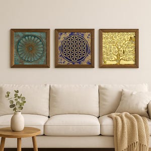 K&ouml;nnte beinhalten: Drei gerahmte Wandkunstwerke. Das erste zeigt ein t&uuml;rkis-goldenes Blumendesign. Das zweite zeigt ein blau-goldenes geometrisches Muster. Das dritte zeigt ein goldenes Baumdesign. Alle in braunen Holzrahmen.
