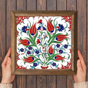 May include: Square framed tile with a floral design. The tile features red tulips, blue and red flowers, and green leaves on a white background. The frame is made of wood.