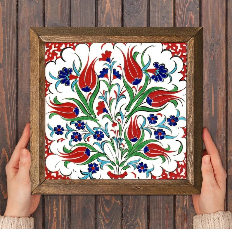 May include: Square framed tile with a floral design. The tile features red tulips, blue and red flowers, and green leaves on a white background. The frame is made of wood.