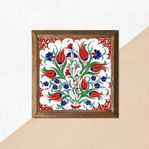 May include: Square framed artwork featuring a floral design. The artwork showcases a white background with a vibrant pattern of red tulips, blue flowers, and green leaves. The frame is made of dark brown wood, adding a classic touch to the piece.