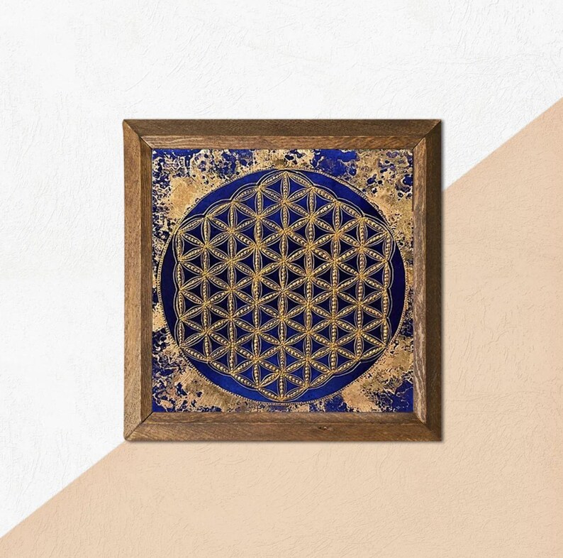 K&ouml;nnte beinhalten: Quadratische Holzrahmen-Kunst mit einem goldenen und blauen geometrischen Design. Das Kunstwerk hat eine dunkelblaue kreisf&ouml;rmige Mitte mit einem goldenen Blume des Lebens-Muster. Der Hintergrund hat einen goldenen Textureffekt. Der Rahmen ist aus braunem Holz.