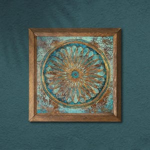 K&ouml;nnte beinhalten: Quadratische Wandkunst mit Holzrahmen mit einem teal- und goldfarbenen Blumendesign. Das Kunstwerk hat ein verwittertes, strukturiertes Aussehen. Das florale Design ist zentriert und von einem kreisf&ouml;rmigen Rand umgeben. Der Rahmen besteht aus Naturholz.