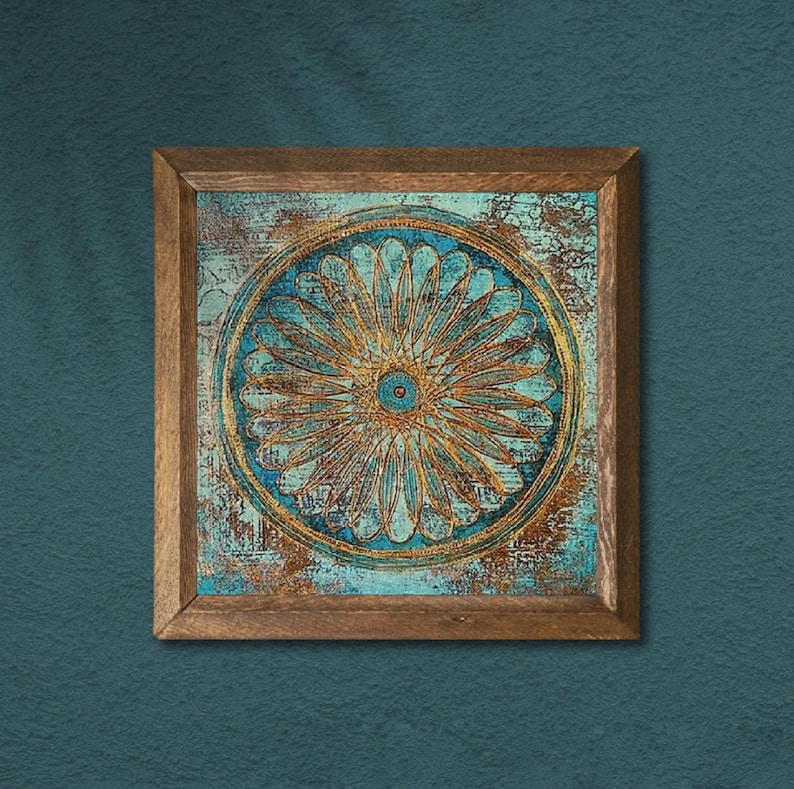 K&ouml;nnte beinhalten: Quadratische Wandkunst mit Holzrahmen mit einem teal- und goldfarbenen Blumendesign. Das Kunstwerk hat ein verwittertes, strukturiertes Aussehen. Das florale Design ist zentriert und von einem kreisf&ouml;rmigen Rand umgeben. Der Rahmen besteht aus Naturholz.