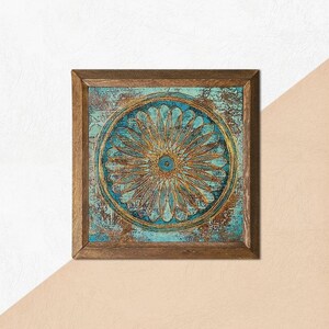 K&ouml;nnte beinhalten: Quadratische gerahmte Wandkunst mit einem t&uuml;rkis-goldenen Blumendesign. Das Kunstwerk hat ein verwittertes, strukturiertes Aussehen mit einem Holzrahmen. Das zentrale Design ist ein detailliertes, kreisf&ouml;rmiges Blumenmuster mit einem goldenen Zentrum.